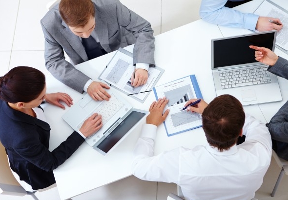 Imagem de uma reunião de planejamento da equipe de uma empresa. Funcionários sentado em volta de uma mesa com notebooks e anotações.